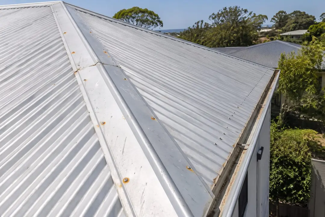 Corrugated metal roof with rust spots around the screws on the ridge capping
